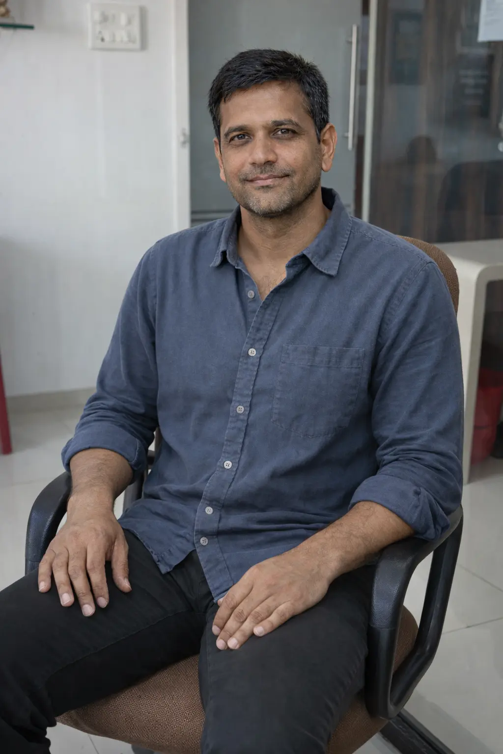 Bhavik wearing a blue shirt sitting on a chair indoors.